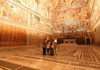 A small group explores an ornately decorated corridor in the Vatican Museums, surrounded by golden-hued ceilings and Renaissance artwork.